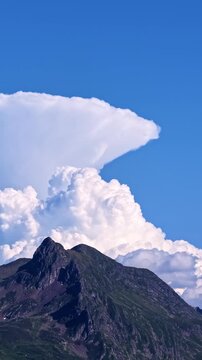 Large cumulonimbus cloud with a distinct pileus cloud cap above a mountain in France, showing towering cloud formations and the surrounding sky - vertical shot