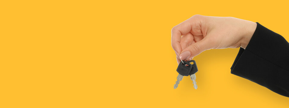 Woman shows car keys in hand against yellow background