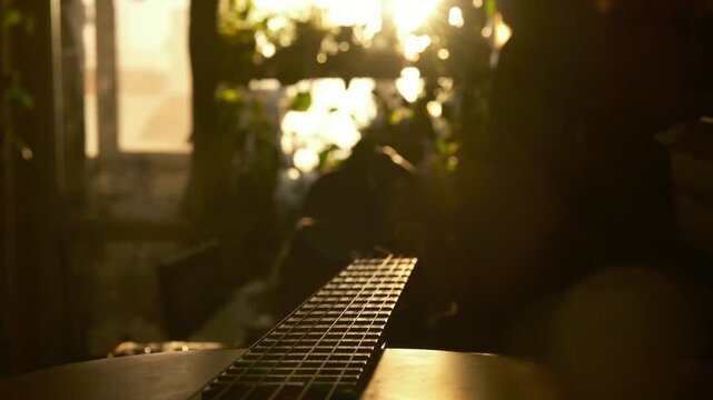Cinematic close-up of an acoustic guitar in warm golden sunset light inside a cozy interior. The camera slowly moves along the strings and wooden body while soft natural sunlight