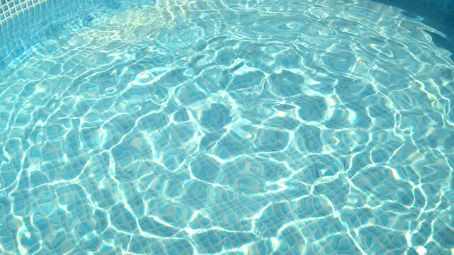 Clear swimming pool water with shimmering sunlight reflections over tiled floor.