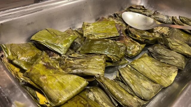A mouth-watering close-up shot of authentic Bhetki Paturi&mdash;barramundi fish coated in mustard paste and mustard oil, steamed in a banana leaf, served at a grand wedding reception in Bengal, India.