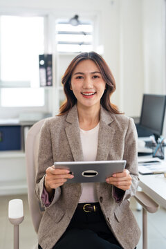 Professional business woman looking at online trade app. ASian woman holding digital tablet using fintech tab application at workplace in office.