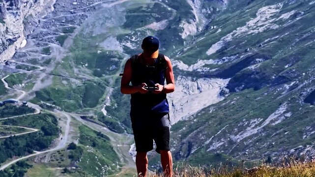 Drone operator standing on a mountain peak, piloting a quadcopter with a controller