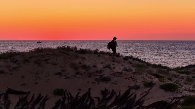 Silhouette of man with backpack walking along sandy dune trail at sunset overlooking ocean near Plage des Oc&eacute;anides Capbreton France