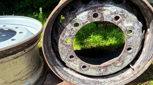 Close-up of rusty old truck wheel rims and worn metal hubs stacked together outdoors on grass in sunlight