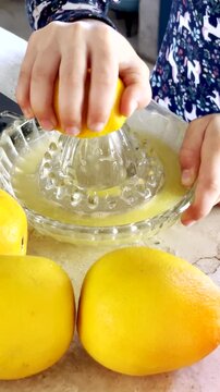 Young girl squeezing fresh orange juice using crystal citrus juicer. Vertical