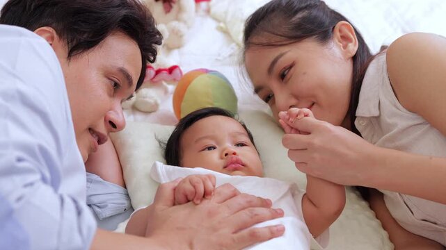 High angle view of a cheerful Asian couple looking at their sweet baby boy on bed. Concept of parenthood, unconditional love, and happy family life.
