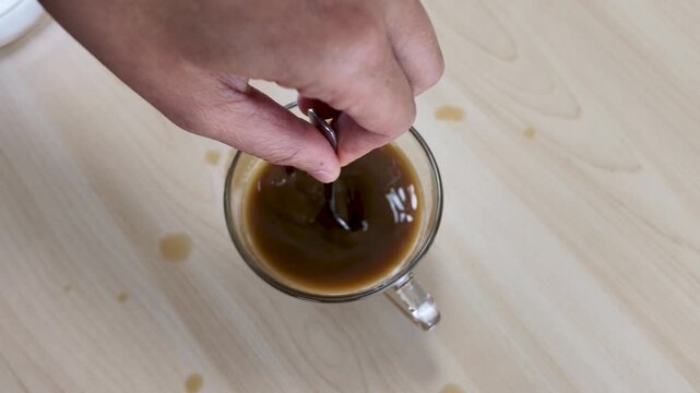 Hand Stirring Hot Black Coffee in Glass Cup on Wooden Table