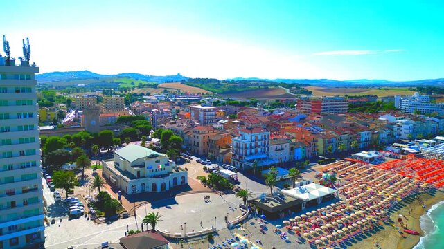 PORTO RECANATI, ITALY - JULY 30, 2025: Aerial truck right pan left arcing shot of Piazza Brancondi. Next to the Adriatic Sea, the square seamlessly connects the historic town center with the promenade