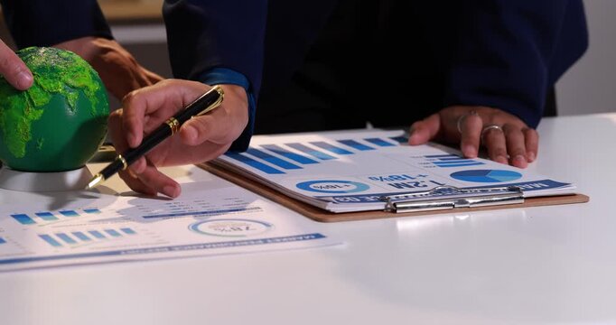 Business people reviewing charts and a globe on a desk, teamwork, planning, and global strategy for finance and growth.