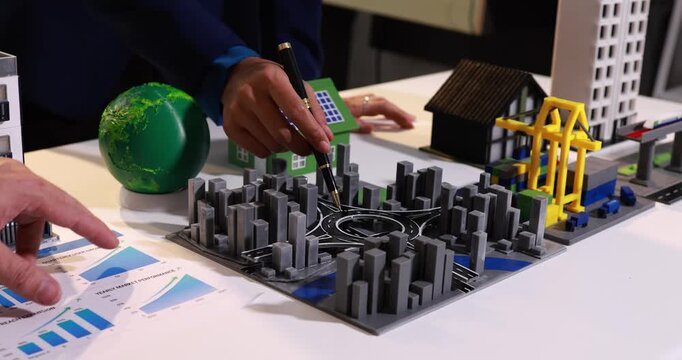 Hands reviewing a city model with charts, a solar house, industrial cranes and buildings on a desk, urban planning, energy and development ideas