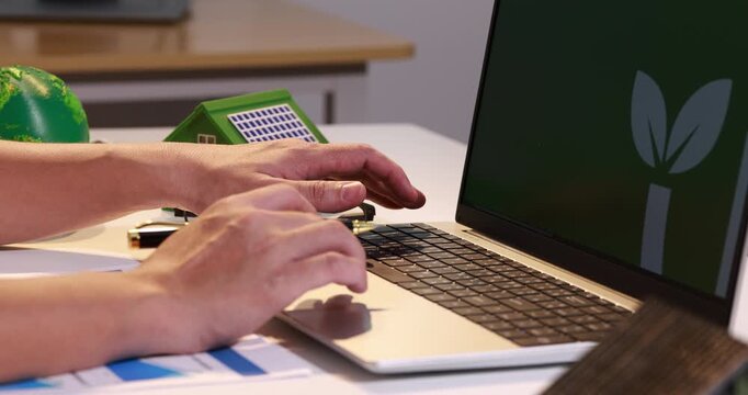 Hands typing on a laptop with esg on the screen, beside green eco models, charts, and a desk setup for sustainable business planning.