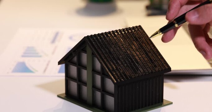 Hand pointing at a small house model with a pen, suggesting home design, real estate planning, or property inspection.