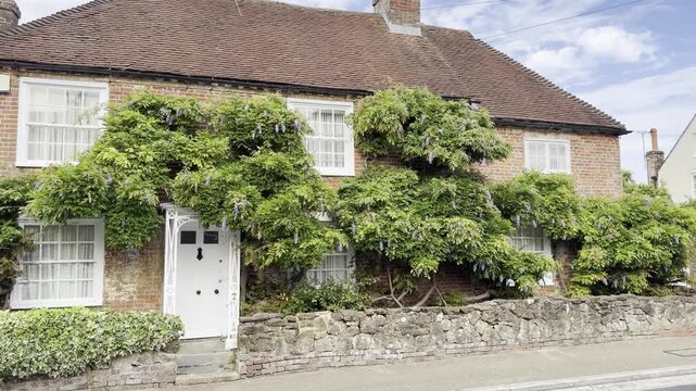 Panning shot of a brick cottage covered in blooming wisteria in Fareham, England