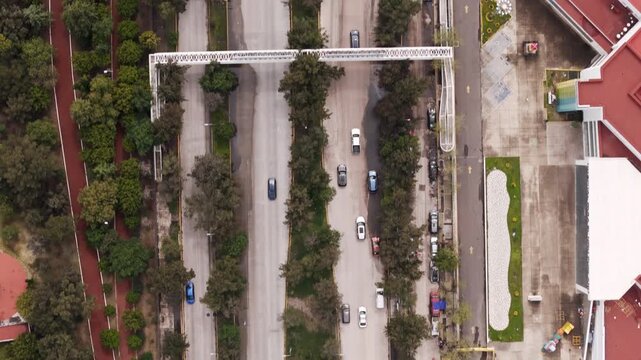 Aerial drone view of a wide, tree-lined boulevard with a curved S-shaped pedestrian bridge in Puebla, Mexico