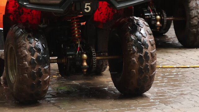 Muddy all terrain vehicle tire closeup wet surface red body off road rugged wheel suspension outdoor travel sport utility vehicle wash mud tire wet pavement cleaning water hose quad bike action