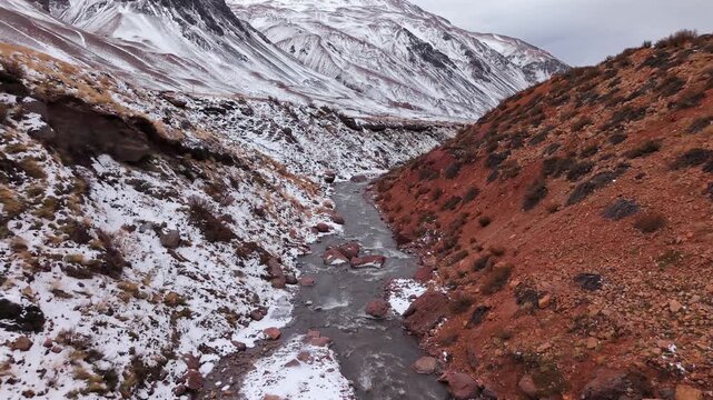 Mendoza River flows through a rugged mountain canyon near Puente del Inca, Las Heras, Mendoza, Argentina, between snow-covered Andean slopes, FPV drone forward flyover gliding.