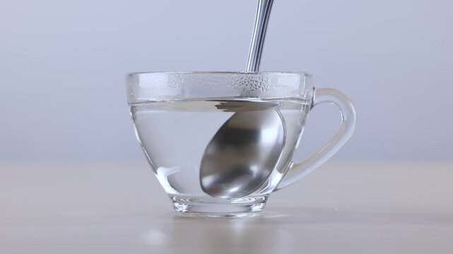 Stirring Clear Liquid in Glass Cup with Metal Spoon