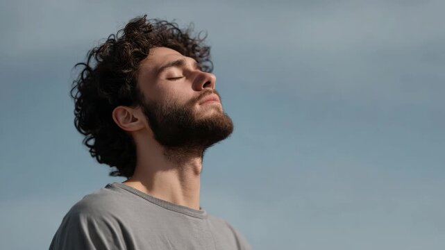 Young Man Enjoying Sunlight Outdoors with Eyes Closed, Peaceful Moment