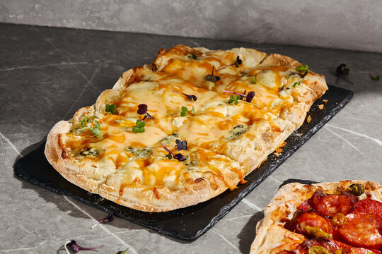 Four cheese Roman pizza with bubbling melted cheese, blue cheese accents and microgreens on a black serving board