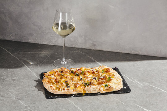 Carbonara Roman pizza with bacon, creamy cheese sauce and microgreens beside a wine glass on a gray copy space background