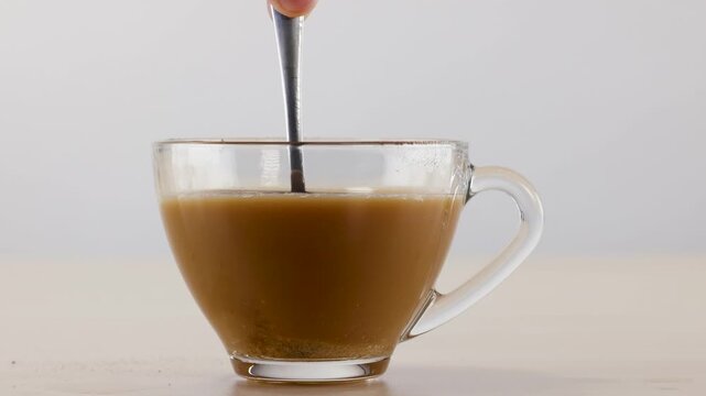 Stirring Coffee with a Metal Spoon in a Clear Glass Mug