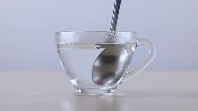 Metal Spoon Stirring Clear Hot Water in Transparent Glass Cup