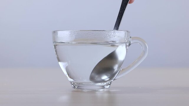 Stirring Clear Hot Liquid in a Glass Cup with Metal Spoon