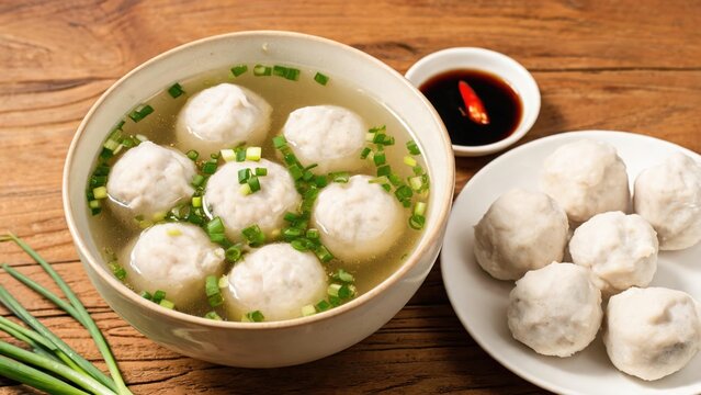 Homemade fish ball clear soup with chopped green onion in ceramic bowl, raw fish balls on side plate, soy chili dipping sauce on rustic wooden table, traditional Chinese street food food photography