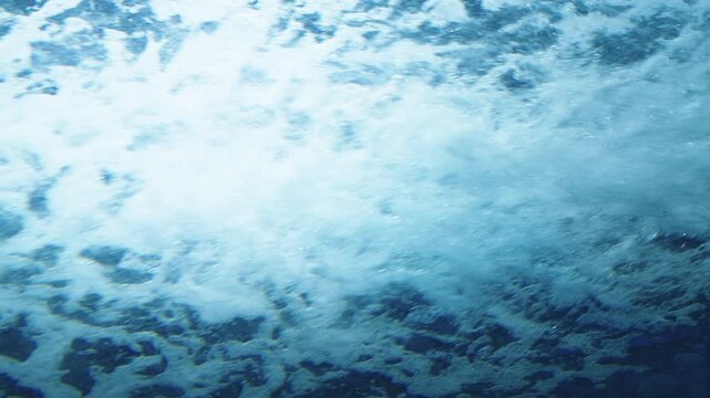 Abstract underwater view of blue ocean water with white foam and bubbles. Bright light shining through surface creating a turbulent aquatic texture. Ideal for nature and background themes.