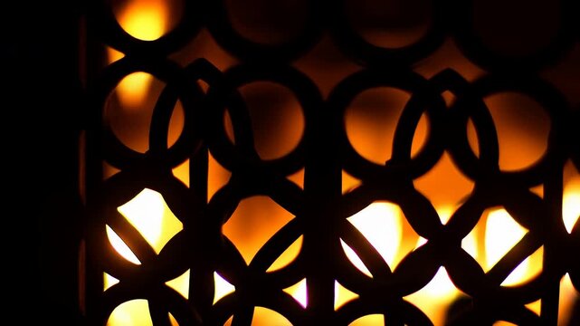 Decorative perforated screen with circular and quatrefoil cutouts silhouetted by warm amber backlight and rising glowing hotspots across repeating geometric surface