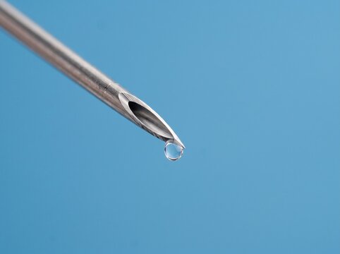 Macro close up of medical hypodermic syringe needle tip with liquid droplet on blue background