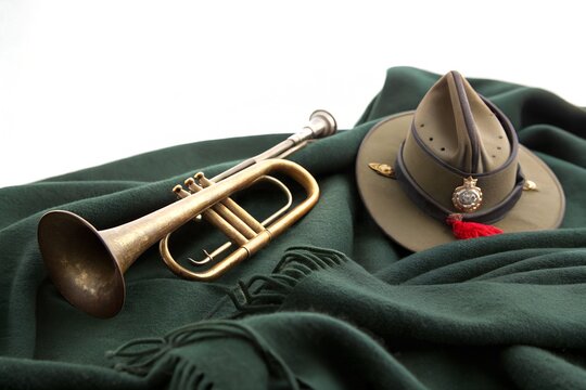 Brass bugle resting beside traditional Australian slouch hat on deep green wool fabric background representing somber memorial tribute during solemn national military remembrance day ceremony