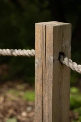 Weathered, textured rustic wooden fence post with thick rope on a blurred natural green background © junky_jess