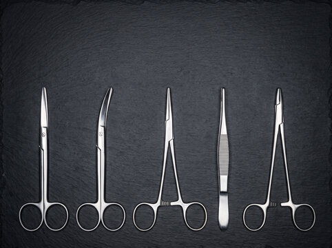 Set of Polished Stainless Surgical Scissors and Clamps Arranged in Ordered Row on Dark Slate Background