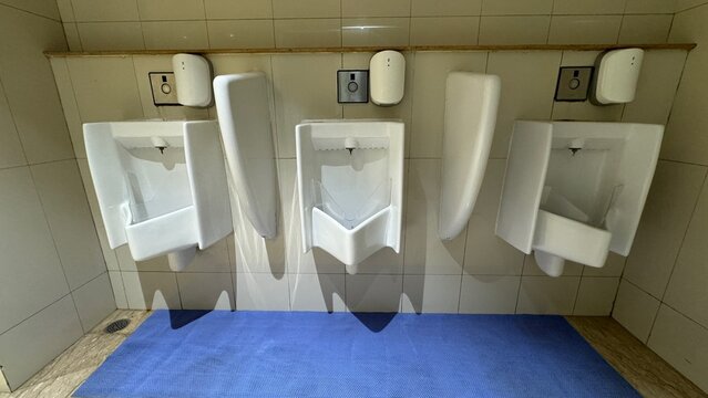 Row of white ceramic male urinals with privacy dividers and automatic sensor flush in public restroom. Clean men toilet facility