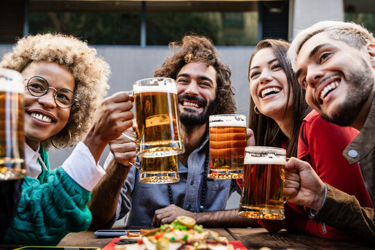 Diverse friends having dinner party together - Multiracial young people having fun toasting beer glasses in brewery pub bar - Happy hour, celebration concept