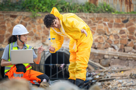 Environmental scientists in hazmat suit and safety gear analyzing water sample at drainage pipe, Industrial specialists checking chemical contamination and water quality near wastewater pipe