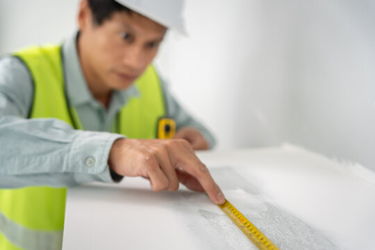 inspector or engineer is inspecting construction and quality assurance check dimension of house by using a tape measurement. Engineers or architects or contactor work to build the house before sell.
