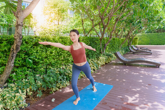 Asian Gen Z woman practicing standing yoga pose in urban park promoting wellness mindfulness and healthy lifestyle