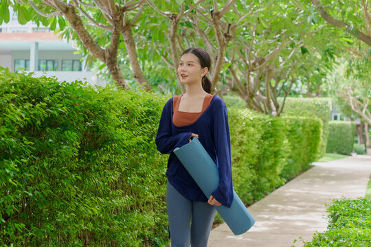Asian Gen Z woman carrying yoga mat walking to park for wellness healthy lifestyle mindfulness and outdoor exercise