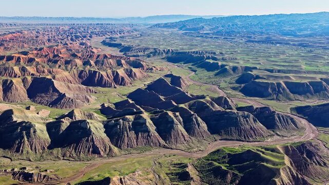 Aerial view of a majestic canyon with a winding riverbed and green grassy valleys along the S101 highway in Xinjiang, China.