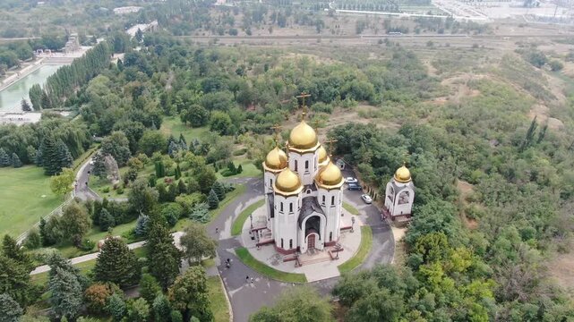 VOLGOGRAD, RUSSIA. AUG 15, 2022: Aerial view of the magnificent Church of All Saints with golden domes surrounded by green trees and memorial park landscape on Mamayev Kurgan.
