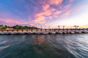 Obraz premium Beautiful sunset view over a wooden pier at Bunaken Island, North Sulawesi, Indonesia. The calm sea reflects soft pastel colors in the sky, creating a peaceful tropical coastal landscape ideal for tra