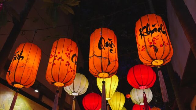 Orange and red cylindrical paper lanterns with calligraphy hanging at night narrow alley