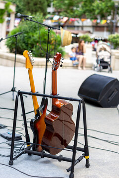 Electric and acoustic guitars on a stand set up for an outdoor street concert.