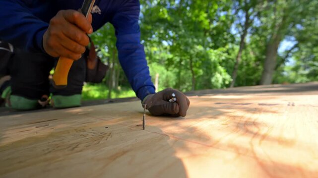 Close up of a roofing contractor hammering nails into plywood roof sheathing during a residential roof replacement.