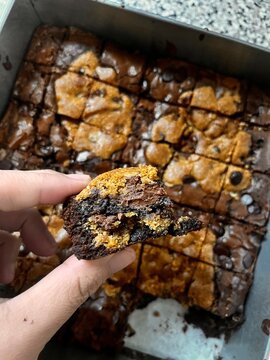 Person holding a slice of freshly baked chocolate chip cookie brownie or brookie