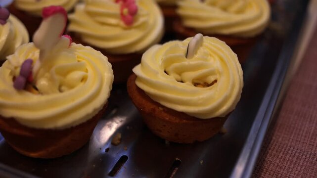A pastry chef skillfully decorates cupcakes with smooth white frosting using a piping bag, creating an exquisite dessert in a bustling professional kitchen filled with mouth-watering aromas. Slow moti