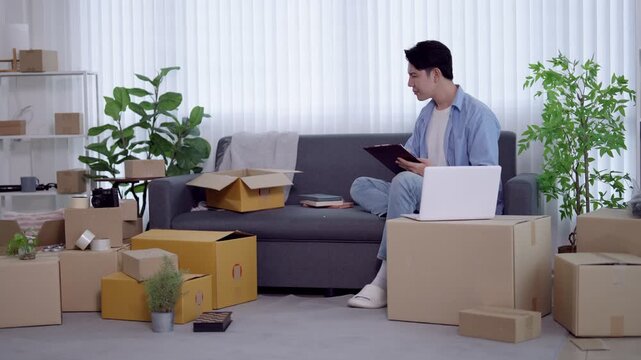 Young Asian entrepreneur checking tablet while managing online business inventory surrounded by shipping parcels at home